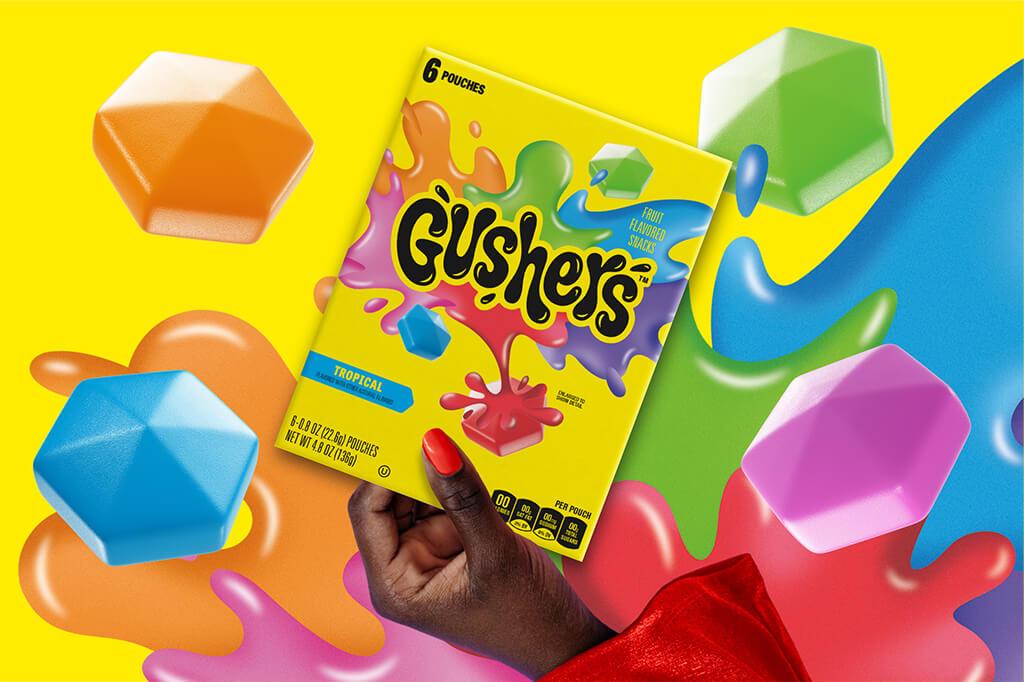 Hand holding Gushers 6 pack Tropical flavor on a yellow background with colorful splats behind it